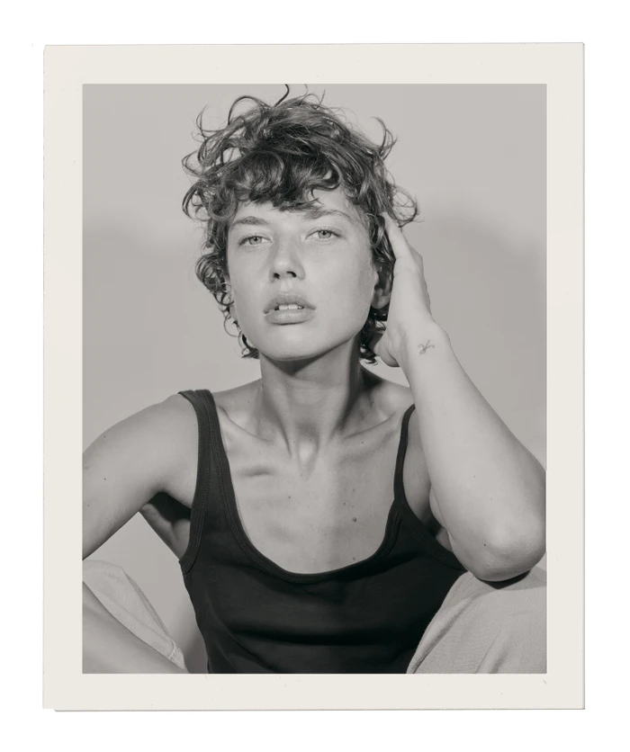 Portrait of a woman with short curly hair wearing a dark tank top against a plain light background