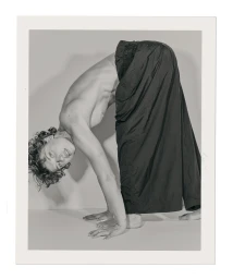 Man with curly hair bending over backwards wearing black trousers on a white studio background
