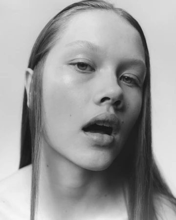 Close-up monochrome portrait of a woman with long straight hair and parted lips against a light background.