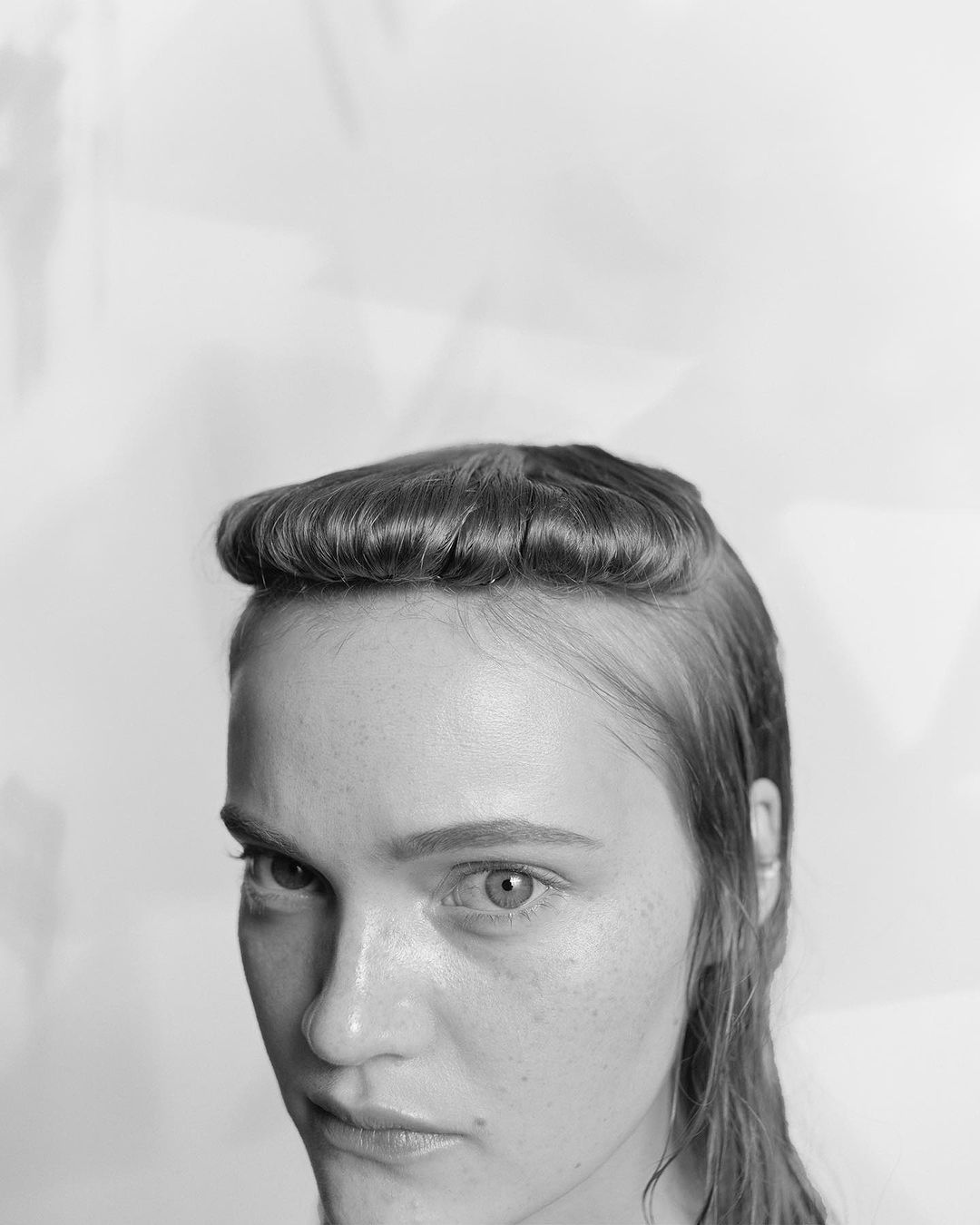 Monochrome portrait of a woman with a rounded fringe hairstyle looking downward against a plain background
