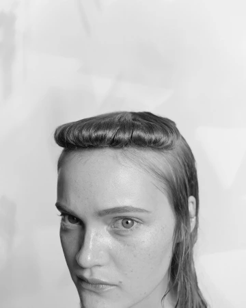 Monochrome portrait of a woman with a rounded fringe hairstyle looking downward against a plain background