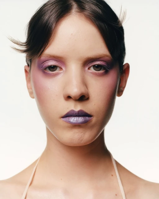 Close-up portrait of a young adult woman with purple eye shadow and metallic purple lipstick on a white background in a photo studio.