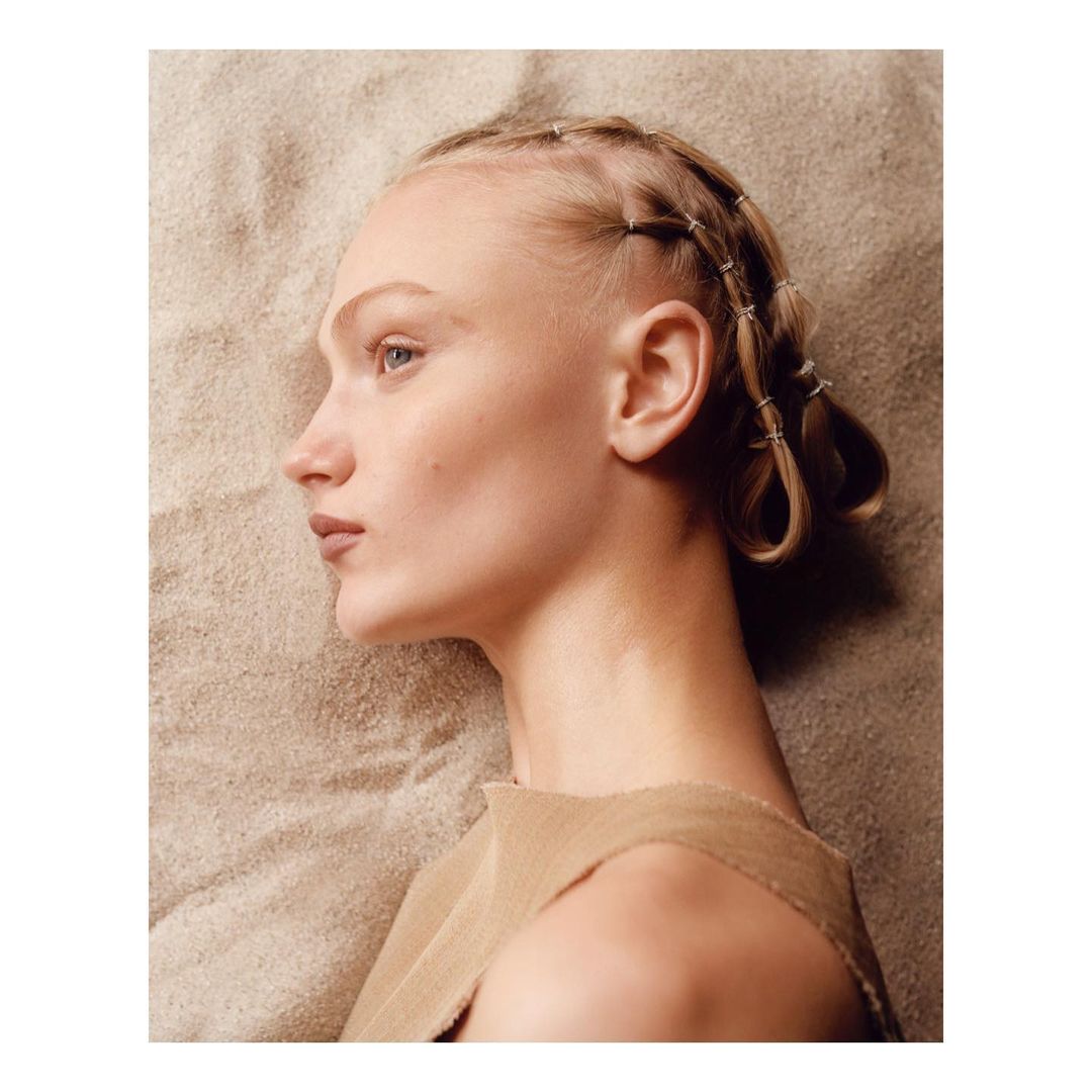 Close-up of a fair-skinned woman with braids, looking serene against a textured beige fabric backdrop, highlighted with natural lighting.