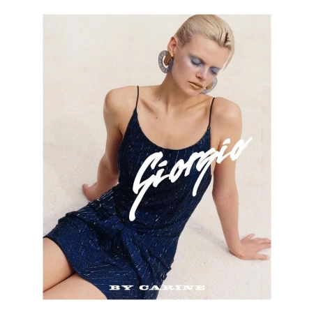 Model in navy blue strapless dress with blonde hair and statement earrings seated against neutral background