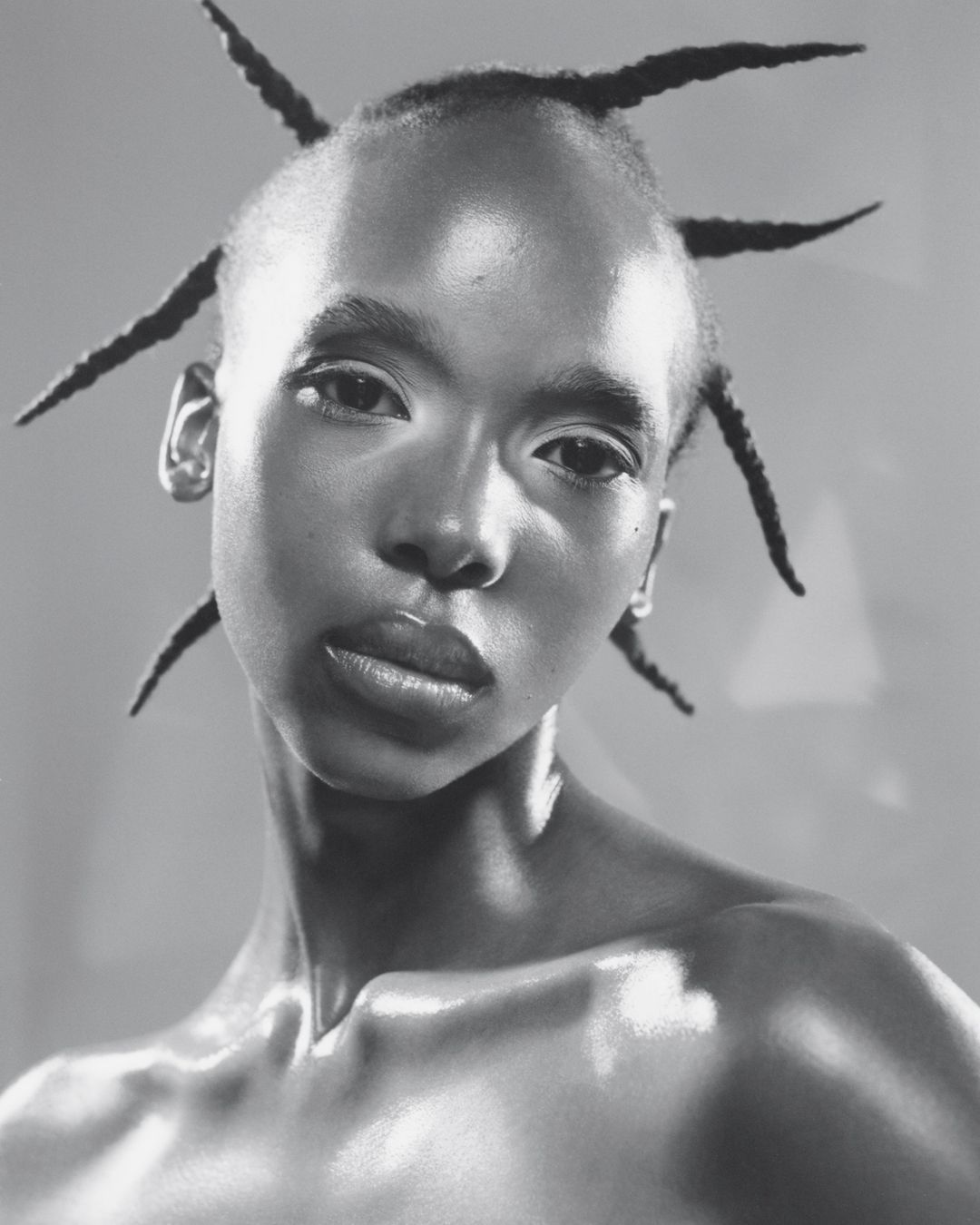 Striking black and white portrait of a young woman with unique hairstyle against a neutral backdrop, emphasizing facial features and textures.