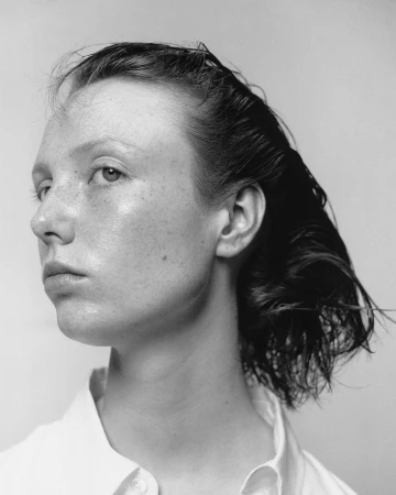 Monochrome portrait of a woman with slicked-back hair and freckles wearing a white collared shirt against a plain light background