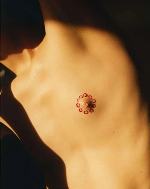 Chest of a bare-chested person in warm lighting, decorated with a pattern of red dots around the nipple area.