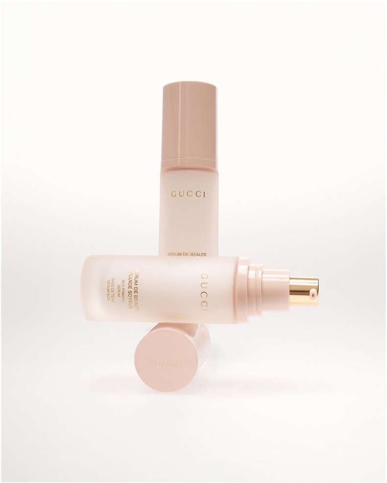 Two pale pink Gucci serum bottles are stacked and overlapping on a white surface, displaying a minimalist aesthetic.