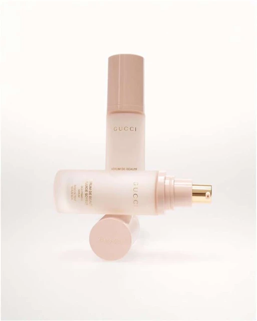 Two pale pink Gucci serum bottles are stacked and overlapping on a white surface, displaying a minimalist aesthetic.