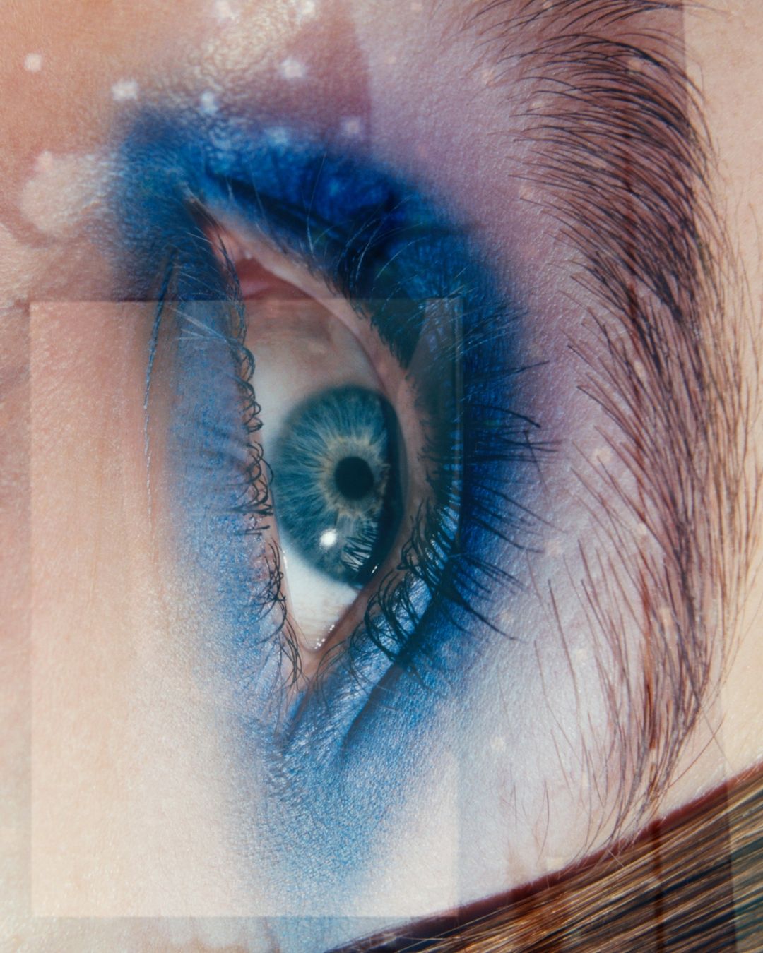 Close-up of a woman's blue eye with bold blue eyeshadow and fair skin, highlighted by a subtle overlay of transparent geometric shapes.