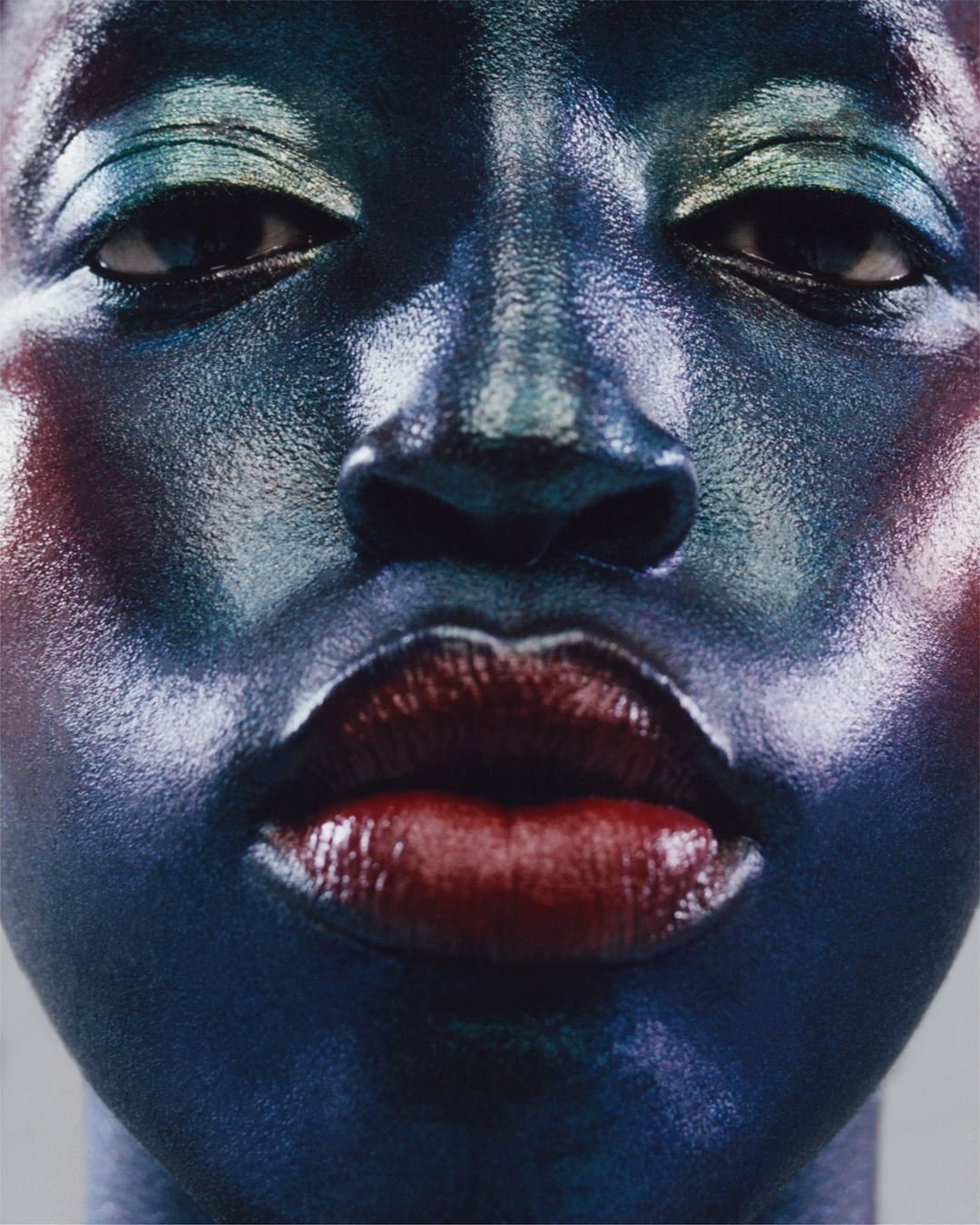 Close-up portrait of a Black female adult face with red lips and blue eyeshadow in a photo studio setting with diffused lighting.