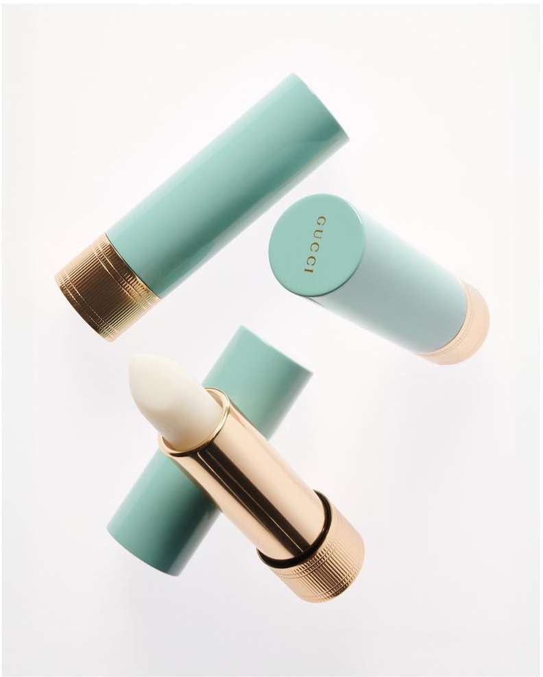 Three aqua and gold Gucci lipsticks are angled on a white background, one is open revealing a white balm.