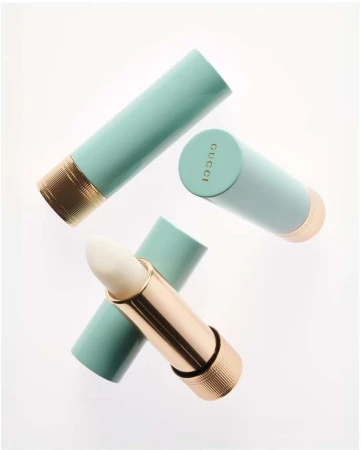 Three aqua and gold Gucci lipsticks are angled on a white background, one is open revealing a white balm.