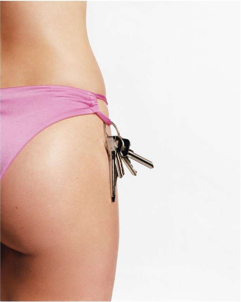 Close-up of an adult female wearing a pink bikini bottom with keys hanging from the side, set against a bright white background.
