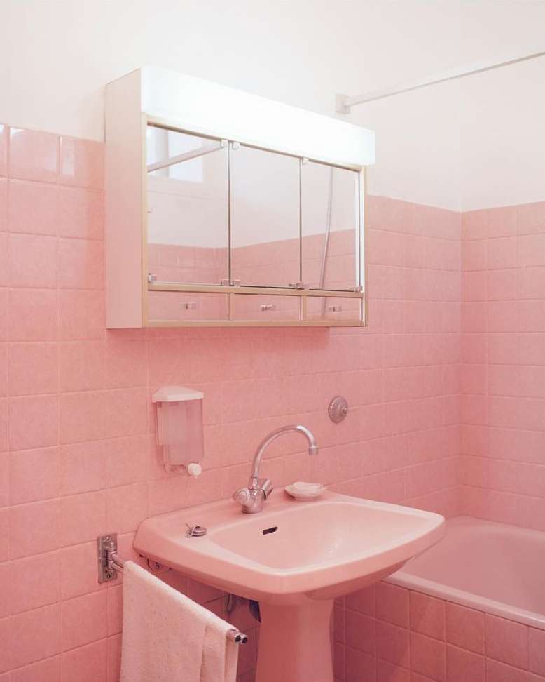 Pink-themed bathroom features a sink, cabinet, mirror, towel, and tiled walls in soft pink hues, creating a retro and clean aesthetic.