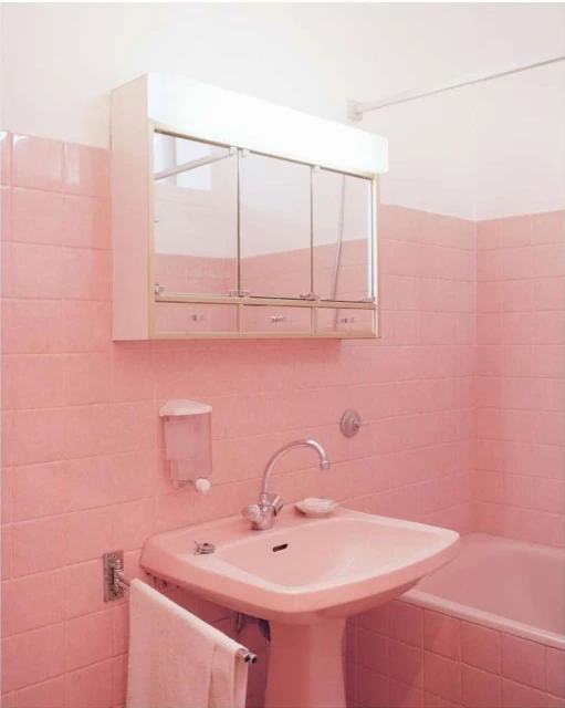Bathroom interior with pink tiled walls, a pedestal sink, mirrored cabinet, and white towel. The scene is brightly lit with a clean, simple aesthetic.