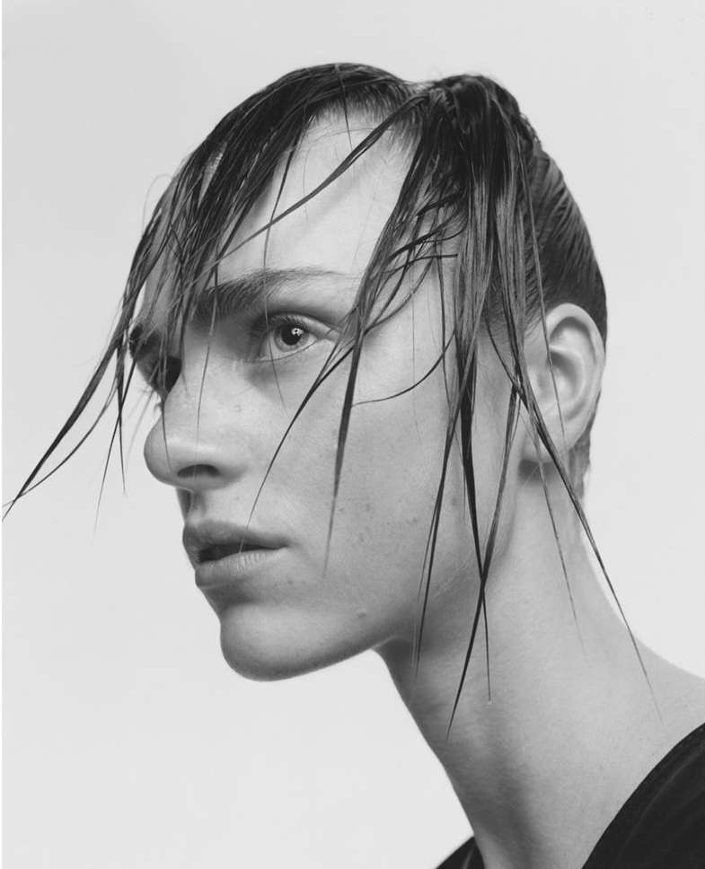 Black and white close-up of a model with slicked-back, wet hair in a high-key studio, showcasing hair and beauty style.