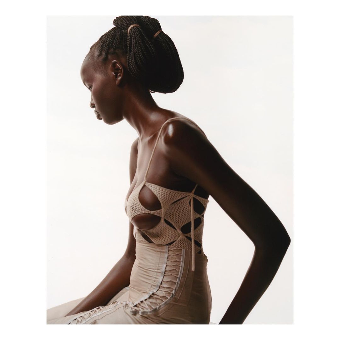 Profile view of a black woman wearing a beige cutout knit top against a bright white background