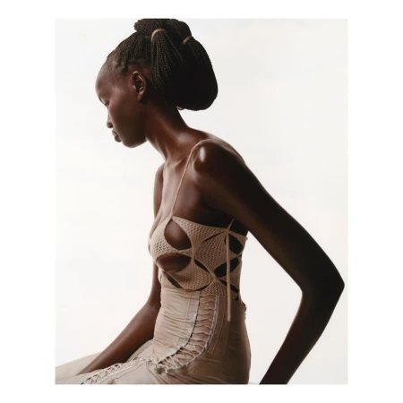 Profile view of a black woman wearing a beige cutout knit top against a bright white background