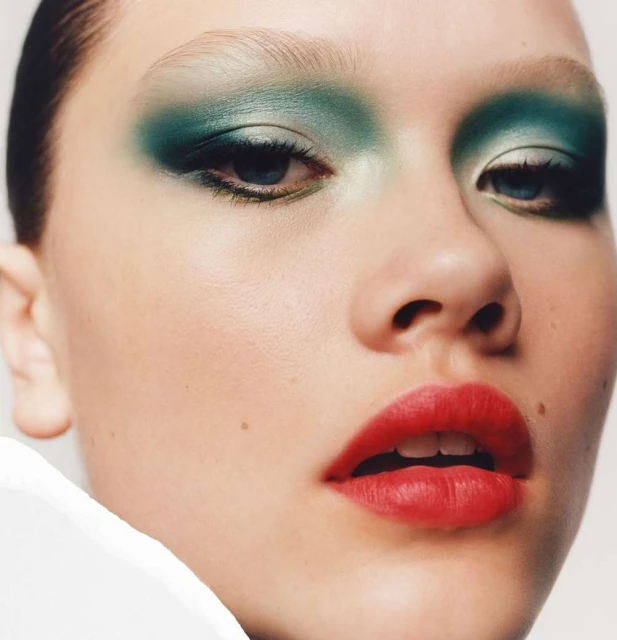 Close-up of a young woman's face with bright green eye shadow and red lipstick, showcasing beauty and cosmetic artistry in a studio setting.