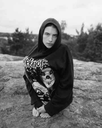 Monochrome portrait of a woman in a black hooded sweatshirt with graphic print kneeling on rocky terrain outdoors