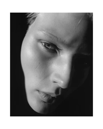 Close-up monochrome portrait of a person with dramatic lighting casting deep shadows across the face.