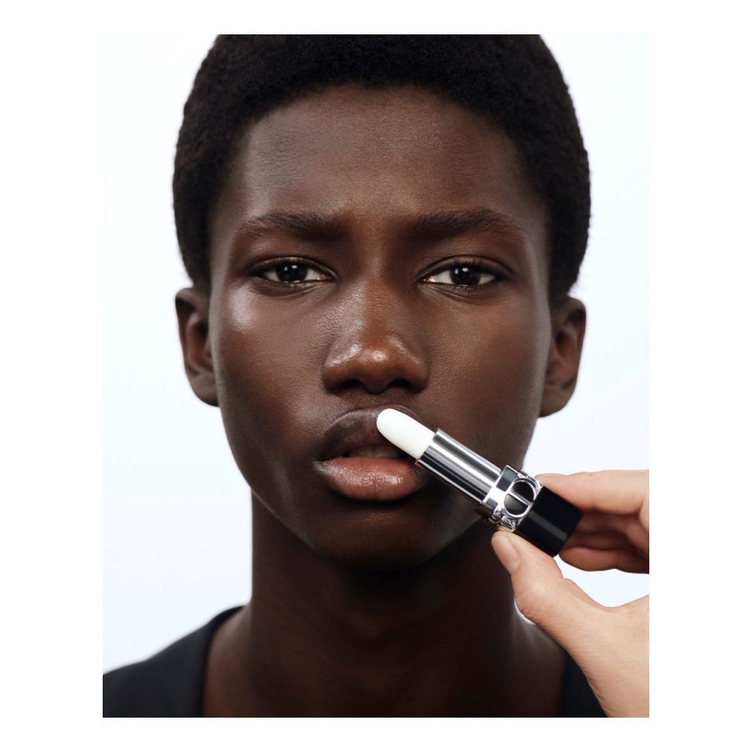 Close-up studio shot of a dark-skinned young adult with a lip balm applicator being held to their lower lip, for beauty and cosmetics.
