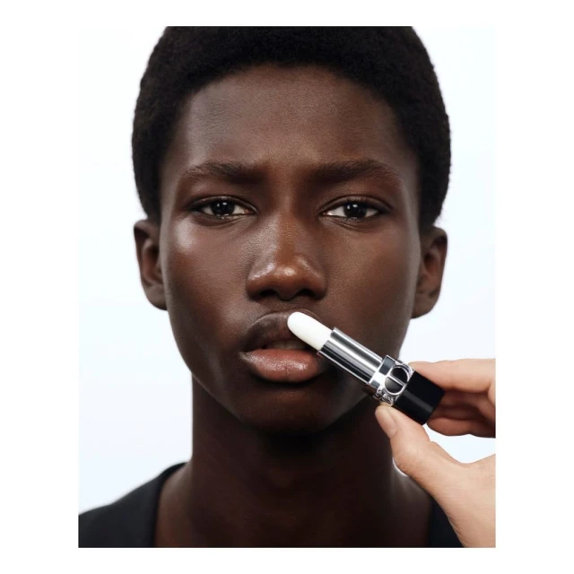 Close-up studio shot of a dark-skinned young adult with a lip balm applicator being held to their lower lip, for beauty and cosmetics.