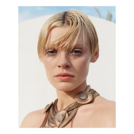 Close-up portrait of a woman with short wet blonde hair wearing a bronze sculptural statement necklace outdoors