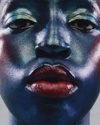 Close-up beauty portrait of a Black woman with glossy metallic blue and green makeup and dark red lips by Benjamin Vnuk.