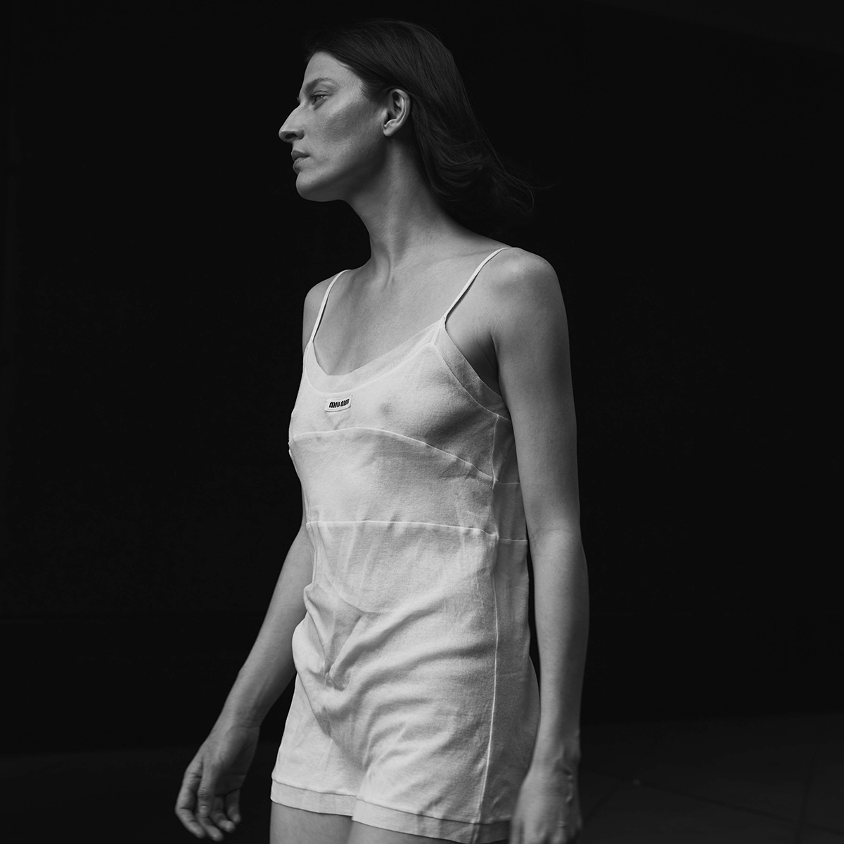 Monochrome shot of an adult woman in a white dress against a dark background, capturing a minimalist fashion aesthetic.