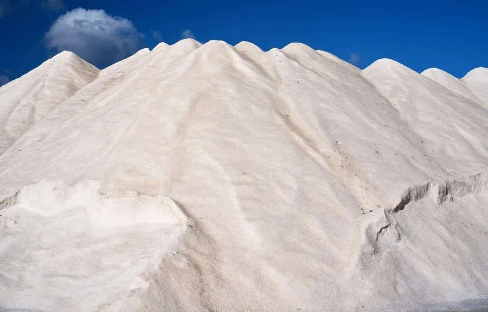 A large pile of salt under a blue sky with a single cloud, creating a stark contrast between the bright white and the deep blue.