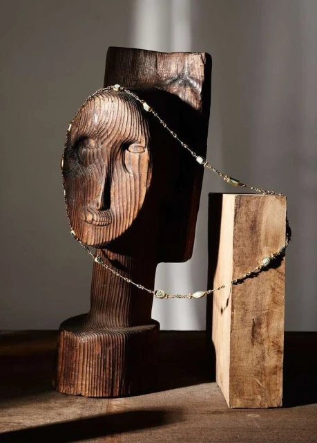 Wooden head sculpture with necklace on a wooden table. Studio lighting on wood texture in an interior setting.