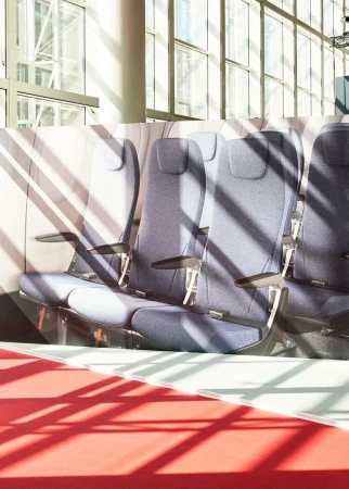 Interior view of rows of airplane seats with overhead sunlight casting striped shadows across the seats and red flooring in the foreground.
