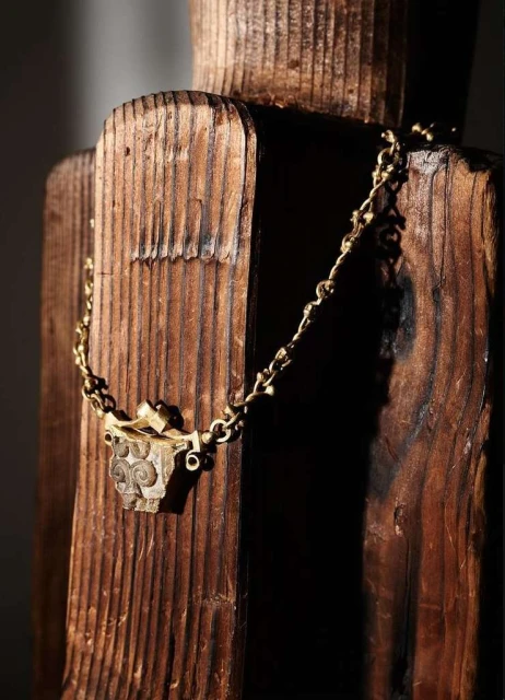 Close-up of a gold chain necklace with a pendant draped over a weathered, dark-stained wooden structure, emphasizing detail and texture.