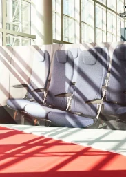Row of blue upholstered passenger seats bathed in strong diagonal patterns of sunlight inside a transport interior.