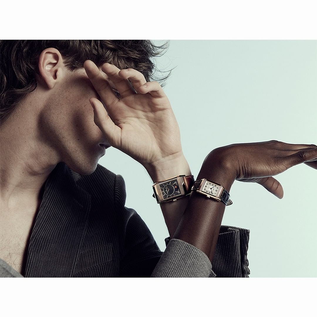 Two people with wristwatches. Light-skinned male partially covers face, dark-skinned female's arm extends to the right, soft lighting.