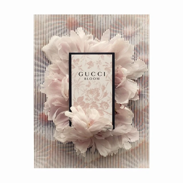 Gucci Bloom perfume product shot featuring a bottle surrounded by light pink peony flowers on a striped background. Fashion, beauty.