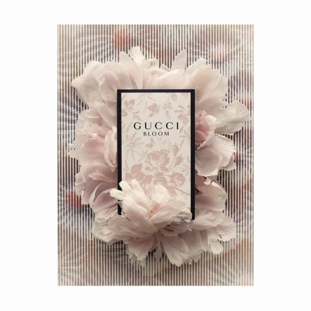 Gucci Bloom perfume product shot featuring a bottle surrounded by light pink peony flowers on a striped background. Fashion, beauty.