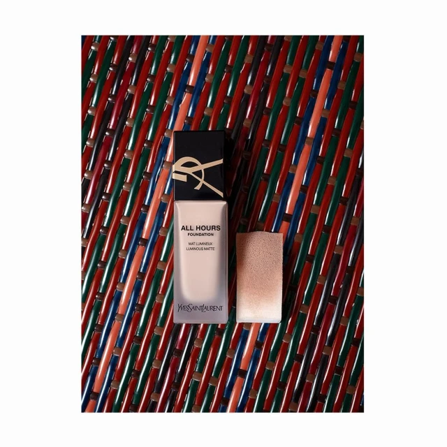Yves Saint Laurent All Hours Foundation bottle with applicator, product shot on a textured multicolored surface, makeup and beauty.