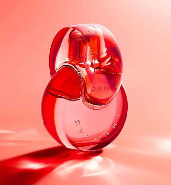 Elegant studio shot of Bulgari Omnia perfume bottle, highlighting its unique shape and vibrant red tones against a matching backdrop.