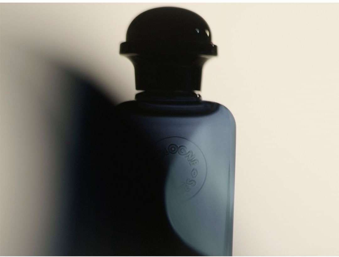 Close-up studio shot of a sleek blue cologne bottle with a dark cap, showcasing minimalist design and contrasting light and shadow.