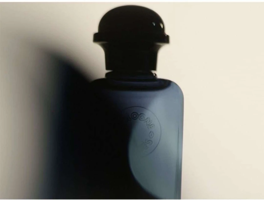 Close-up studio shot of a sleek blue cologne bottle with a dark cap, showcasing minimalist design and contrasting light and shadow.