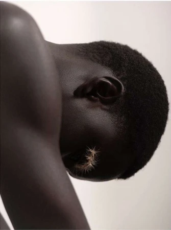 Close-up portrait of a dark-skinned adult with short hair and spiky decorative elements applied to the cheek against a plain background.