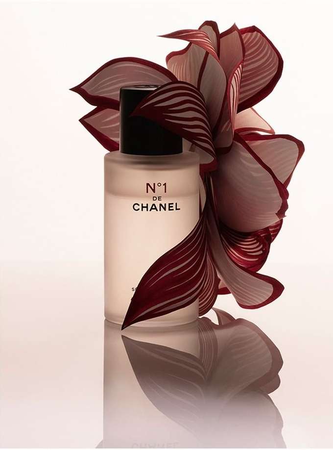 Chanel N°1 de Chanel bottle with floral accents, product shot. Black cap, white bottle, red and pink flower petals in arrangement.