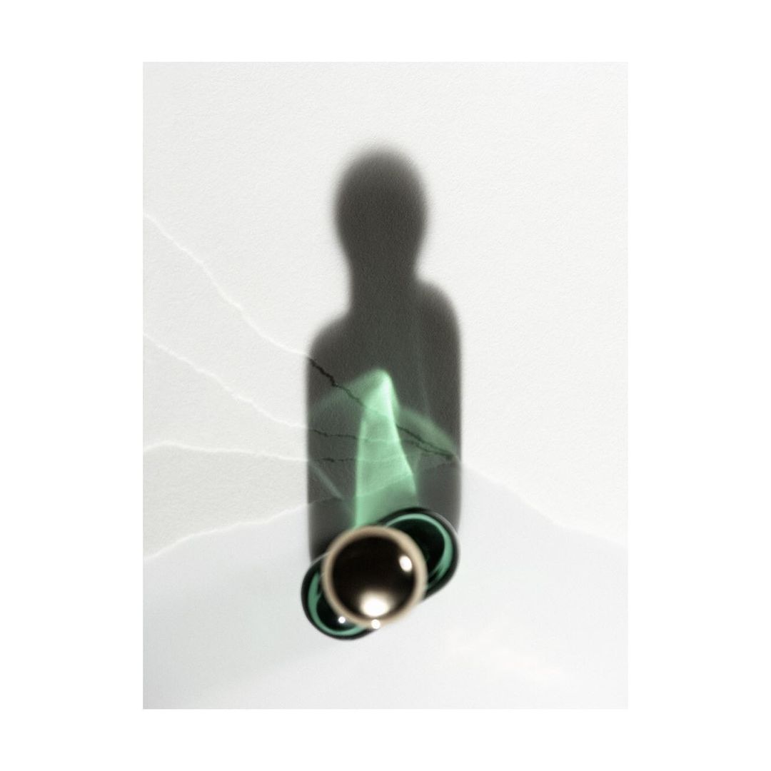 A modern still life photograph with a glass bottle casting a dark shadow on a plain white background with subtle light leaks and textures.