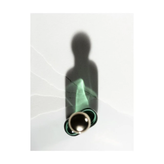 A modern still life photograph with a glass bottle casting a dark shadow on a plain white background with subtle light leaks and textures.