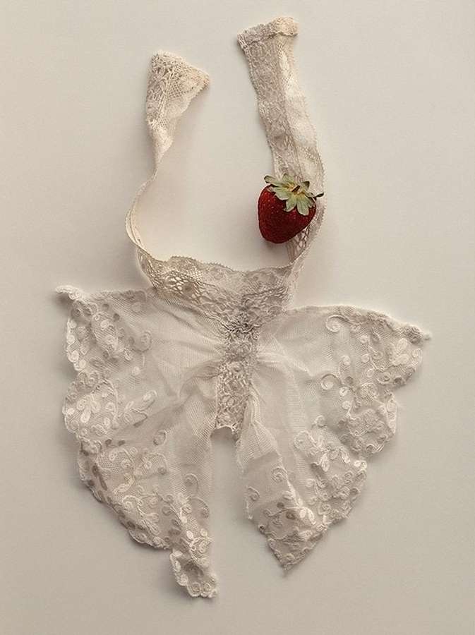 Lace bralette top with strawberry accent on a cream-colored background. Delicate and feminine fashion detail still life.