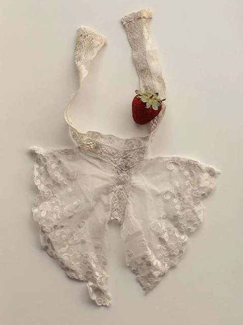 Lace bralette top with strawberry accent on a cream-colored background. Delicate and feminine fashion detail still life.