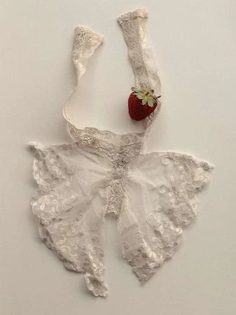 Lace bralette top with strawberry accent on a cream-colored background. Delicate and feminine fashion detail still life.